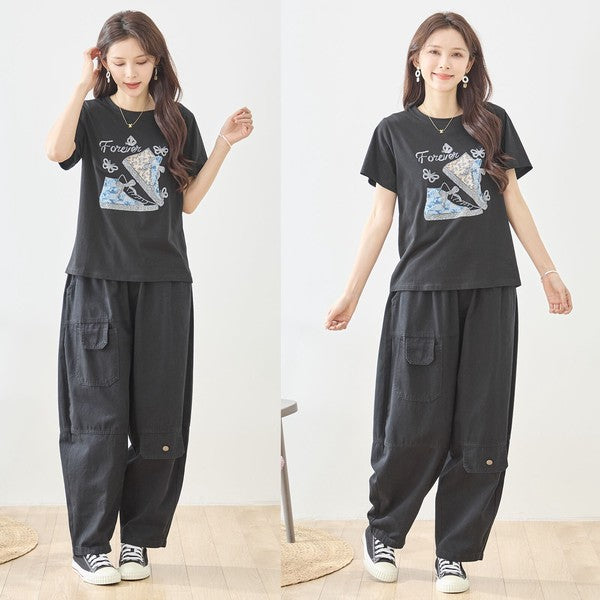 Mikonosublue Storeのラインストーンと異素材パッチワークのスニーカー柄が施された黒の半袖Tシャツを着用した女性