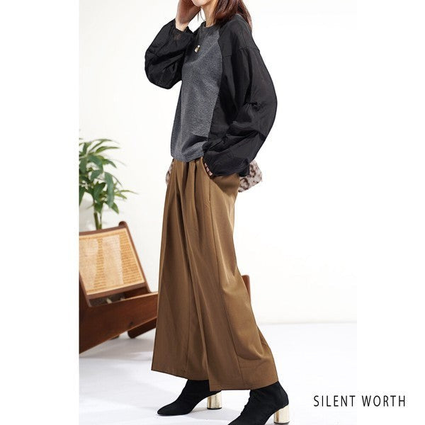 Mikonosublue Store black and grey mixed-material pullover with voluminous raglan tuck sleeves worn with brown trousers