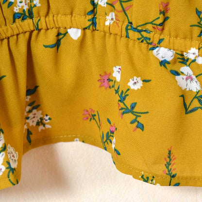 Mikonosublue Storeのマスタードカラーの花柄ジョーゼットブラウス。裾のシャーリングゴムがペプラム風のシルエットを作る。
