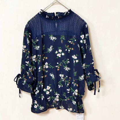 Mikonosublue Storeのネイビー花柄ジョーゼットブラウス。デコルテのシアーレースと袖口のリボンが上品な七分袖トップス。