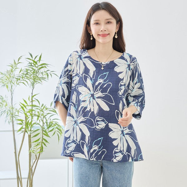 Mikonosublue Storeのネイビー地に白い大きな花柄がプリントされた綿100%のゆったりとしたドルマン袖トップスを着た女性