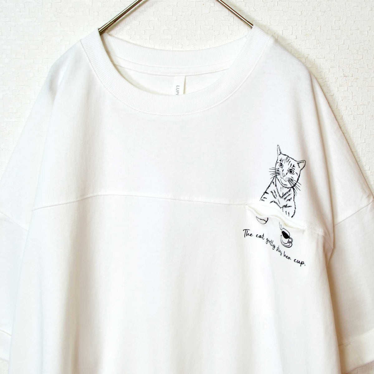 Mikonosublue Storeの白い綿100%天竺チュニックTシャツ。胸元に可愛い猫のイラストと英字がプリントされたゆったりとしたドロップショルダーデザイン。