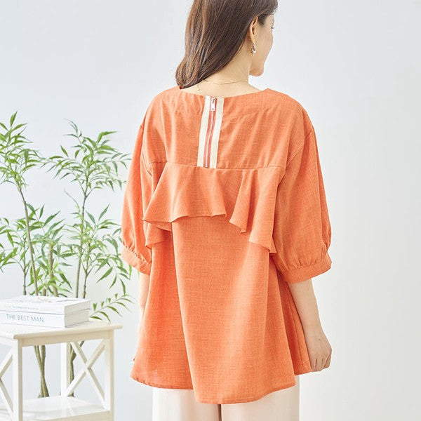 Mikonosublue Storeのバックフリルとファスナーが特徴的なオレンジ色の5分袖Aライントップスを着用した女性の後ろ姿