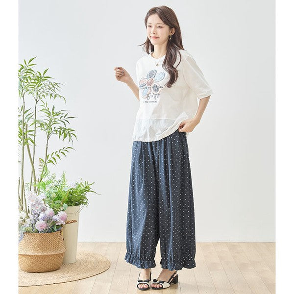 Mikonosublue Storeのネイビーのピンドット柄ワイドパンツ。裾のフリルとゆったりしたシルエットが特徴で、モデルが白Tシャツと合わせて着用しています。
