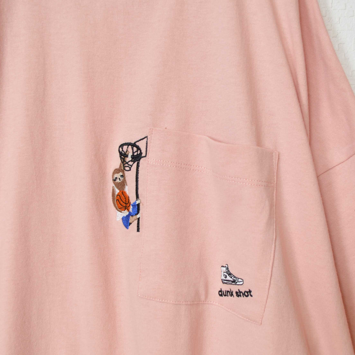 Mikonosublue Storeのピンク色の綿100%天竺Tシャツ。胸ポケットにバスケットボールをする動物の刺繍入り。