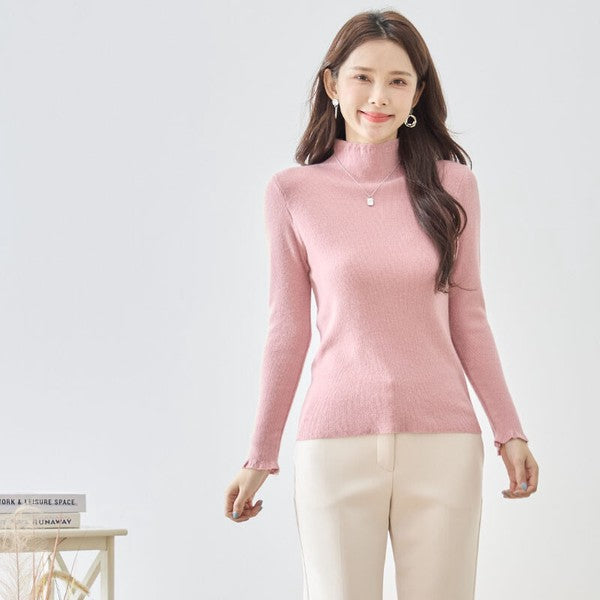 Mikonosublue Storeのピンク色のフリルハイネックリブニットプルオーバーを着用した女性