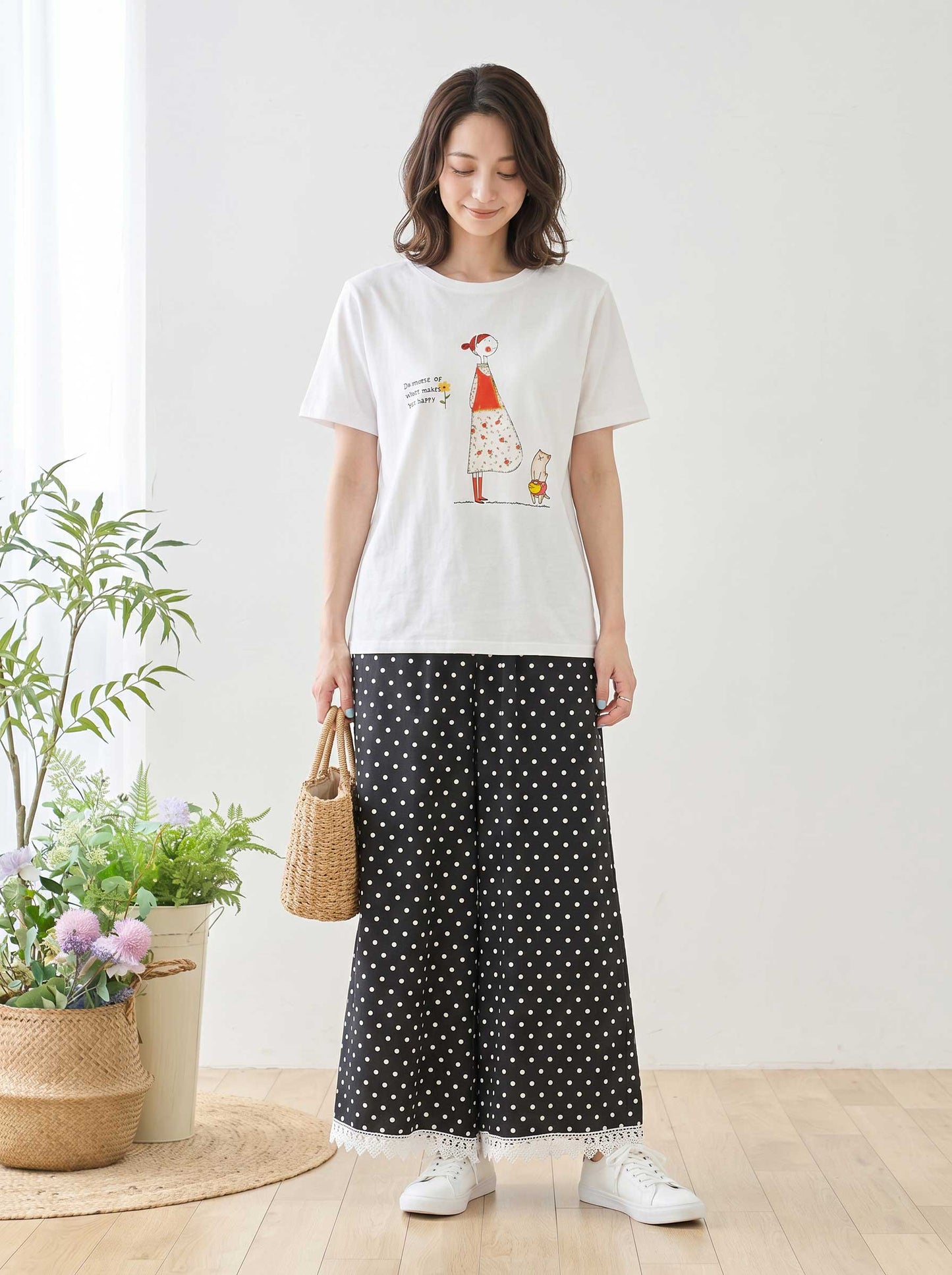 Mikonosublue Storeのポルカドット柄ワイドパンツ。裾に白いクロシェレースをあしらった黒のゆったりとしたパンツを、白いイラストTシャツとスニーカーで着こなす女性。