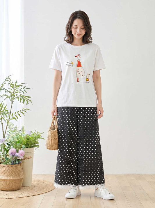 Mikonosublue Storeのポルカドット柄ワイドパンツ。裾に白いクロシェレースをあしらった黒のゆったりとしたパンツを、白いイラストTシャツとスニーカーで着こなす女性。