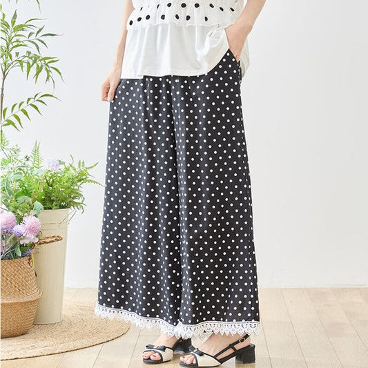Mikonosublue Storeのポルカドット柄ワイドパンツ。裾に白いクロシェレースをあしらった黒のレーヨン混素材で、ゆったりとしたシルエットが特徴。