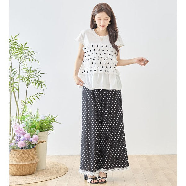 Mikonosublue Storeのポルカドット柄ワイドパンツ。裾に白いクロシェレースをあしらった黒のゆったりとしたパンツを着用した女性。