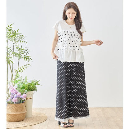 Mikonosublue Storeのポルカドット柄ワイドパンツ。裾に白いクロシェレースをあしらった黒のゆったりとしたパンツを着用した女性。