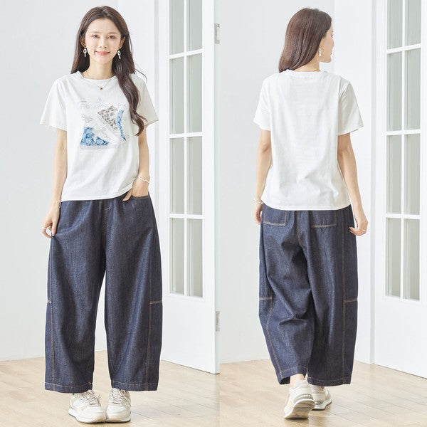 Mikonosublue Storeのラインストーンと異素材パッチワークのスニーカー柄が施されたゆったりとした白い半袖Tシャツを着用した女性