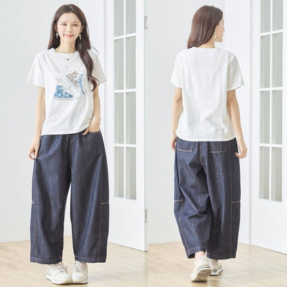 Mikonosublue Storeのラインストーンと異素材パッチワークのスニーカー柄が施されたゆったりとした白い半袖Tシャツを着用した女性