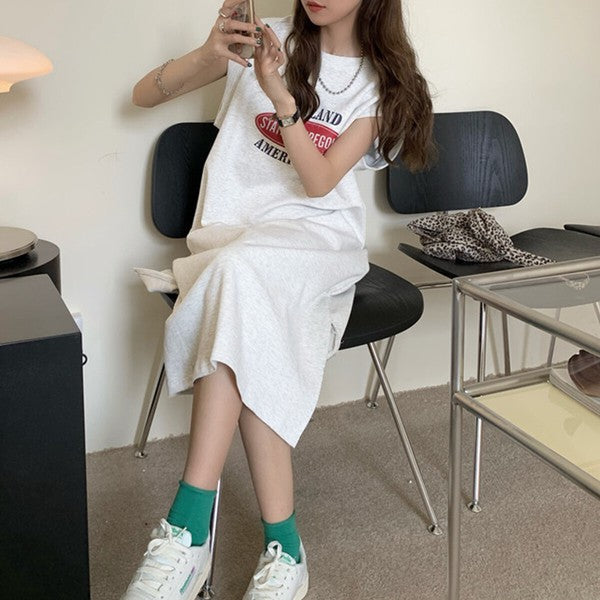 Mikonosublue Storeのグレーのロゴプリント入りフレンチスリーブTシャツワンピース。ゆったりとしたシルエットでサイドスリットがあり、カジュアルな着こなし。