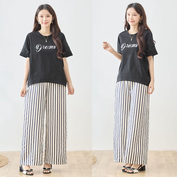 Mikonosublue Storeのストライプ柄ワイドパンツを着用した女性。黒のロゴTシャツと合わせたリラクシーなコーディネート。