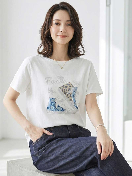 Mikonosublue Storeのラインストーンと異素材パッチワークのスニーカー柄が施されたゆったりとした白い半袖Tシャツを着た女性