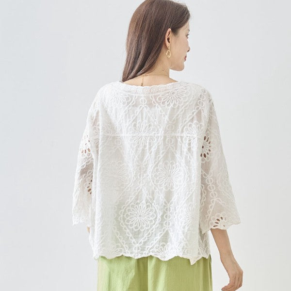 Mikonosublue Storeの白いコットン製カットワーク刺繍ブラウス。七分袖でゆったりとしたシルエットの夏用トップス。