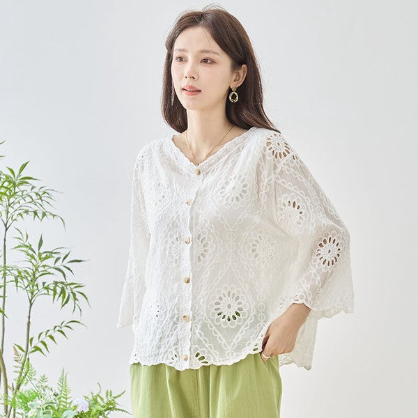 Mikonosublue Storeの白いコットン製カットワーク刺繍ブラウス。Vネックと七分袖が特徴の涼しげな夏用トップスを着用した女性。