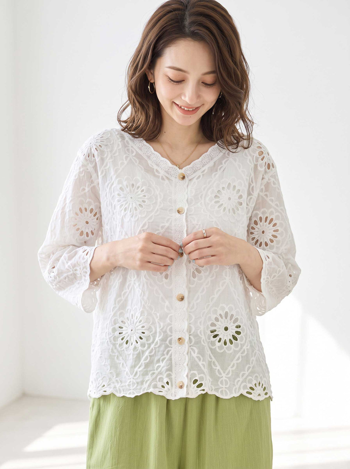 Mikonosublue Storeの白いコットン製カットワーク刺繍ブラウス。Vネックと七分袖で、花柄の透かし模様が涼しげなデザイン。