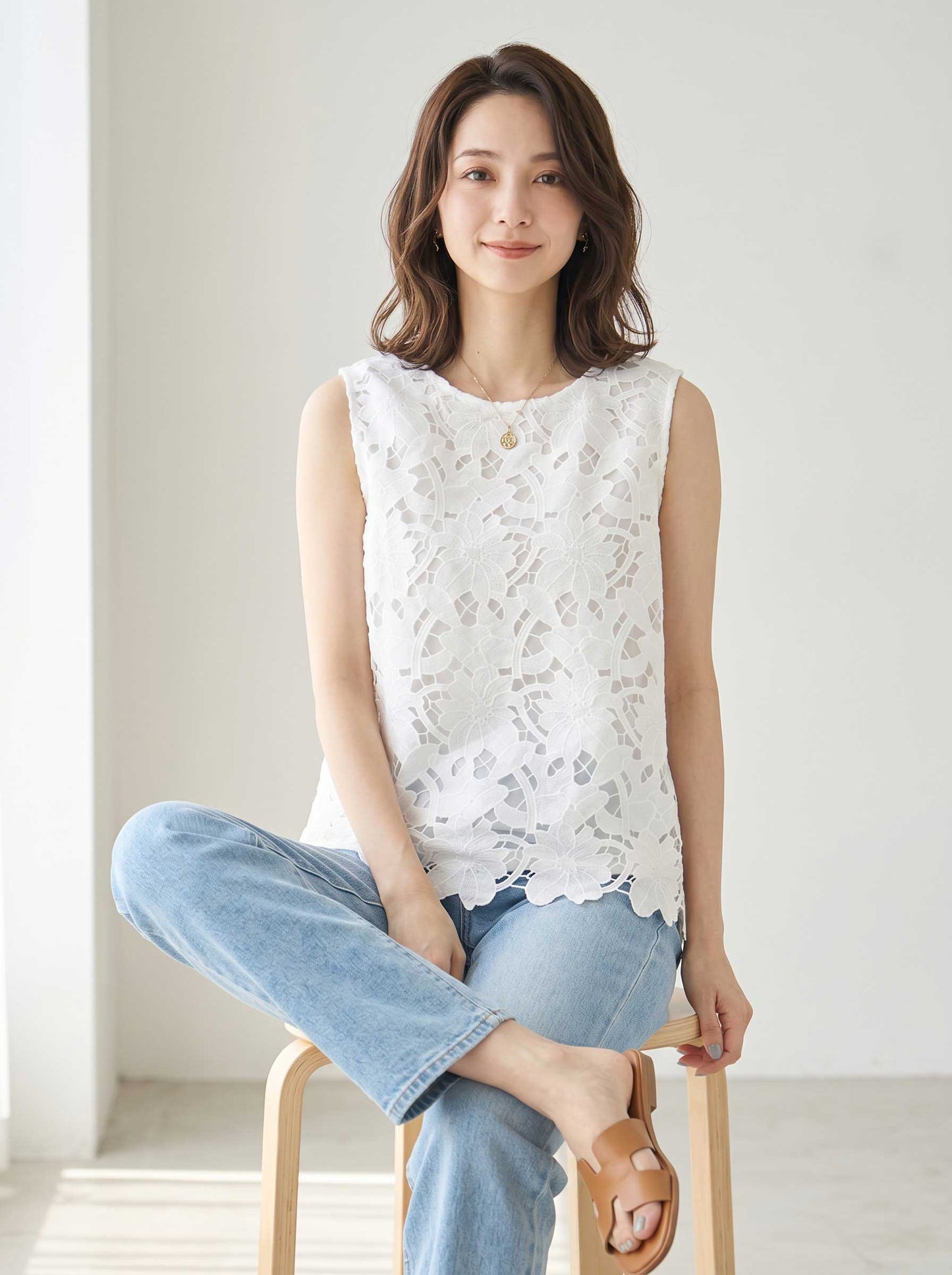 Mikonosublue Storeの白いフラワーカットワークレースのノースリーブトップス。裾はスカラップ仕様で、デニムパンツと合わせた上品なカジュアルスタイル。