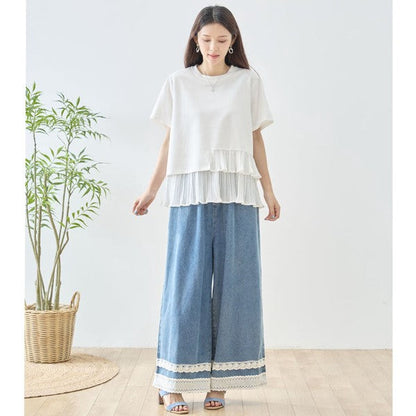 Mikonosublue Storeのホワイトの異素材切り替えTシャツ。裾にアシンメトリーなプリーツフリルをあしらい、ワイドデニムパンツと合わせたフェミニンな夏コーデ。