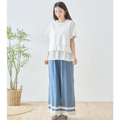 Mikonosublue Storeの裾にプリーツフリルをあしらった異素材切り替えの白い半袖Tシャツを着用した女性