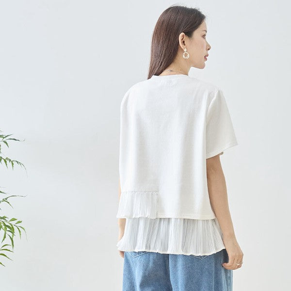 Mikonosublue Storeのホワイトの異素材切り替えTシャツ。裾にアシンメトリーな2段ティアードプリーツフリルをあしらったフェミニンな半袖トップス