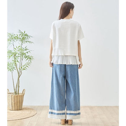 Mikonosublue Storeの裾にアシンメトリーなプリーツフリルをあしらったホワイトの半袖Tシャツを着用した女性のバックスタイル