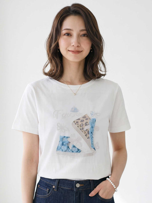 Mikonosublue Storeのラインストーンと異素材パッチワークのスニーカー柄が施された、ゆったりとした白い半袖コットンTシャツを着用した女性