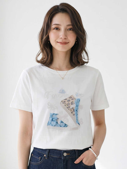 Mikonosublue Storeのラインストーンと異素材パッチワークのスニーカー柄が施された、ゆったりとした白い半袖コットンTシャツを着用するモデル